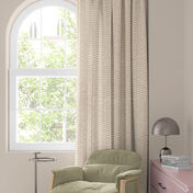 Finestra con tenda floreale colorata in rosso, arancione e blu, poltrona verde e piccolo tavolo con lampada